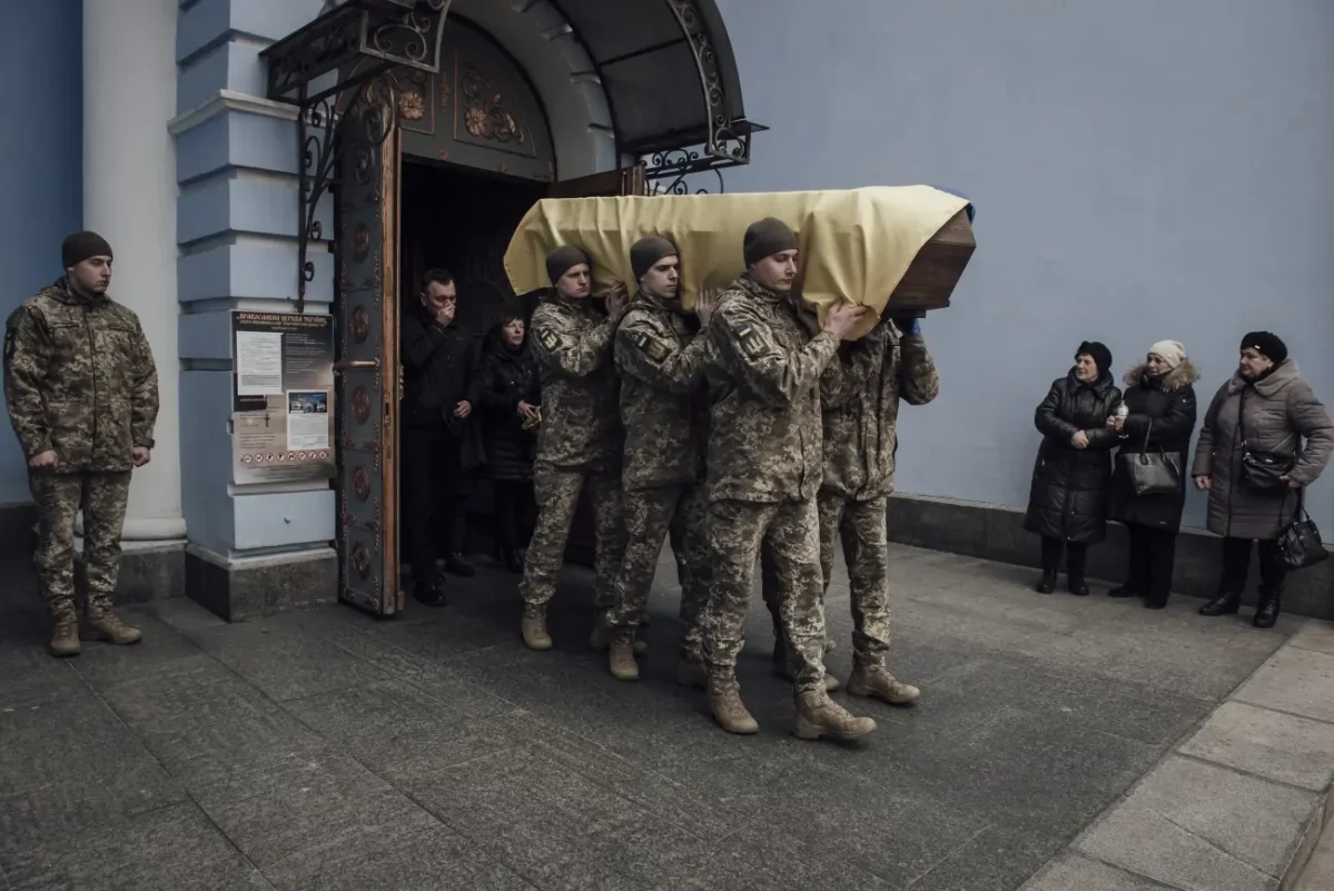 Kyiv, Ukraine, 18 mars 2023. Le cercueil du soldat Herasimchuk est porté hors de l’église par ses camarades de brigade, tandis que ses parents suivent le cortège funéraire. Photo © Adrien Vautier Kyiv, Ukraine, 18 mars 2023. Le cercueil du soldat Herasimchuk est porté hors de l’église par ses camarades de brigade, tandis que ses parents suivent le cortège funéraire. Photo © Adrien Vautier